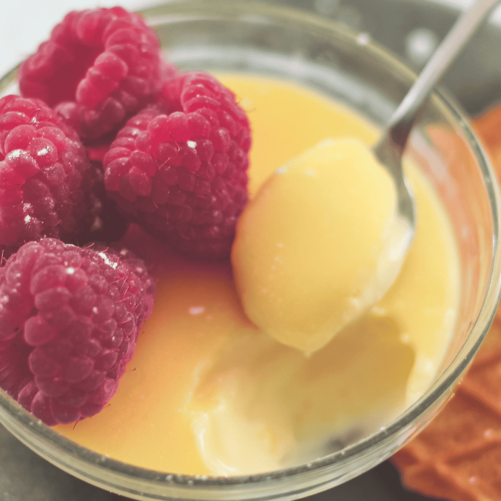 A close up shot of a lemon posset with raspberries.